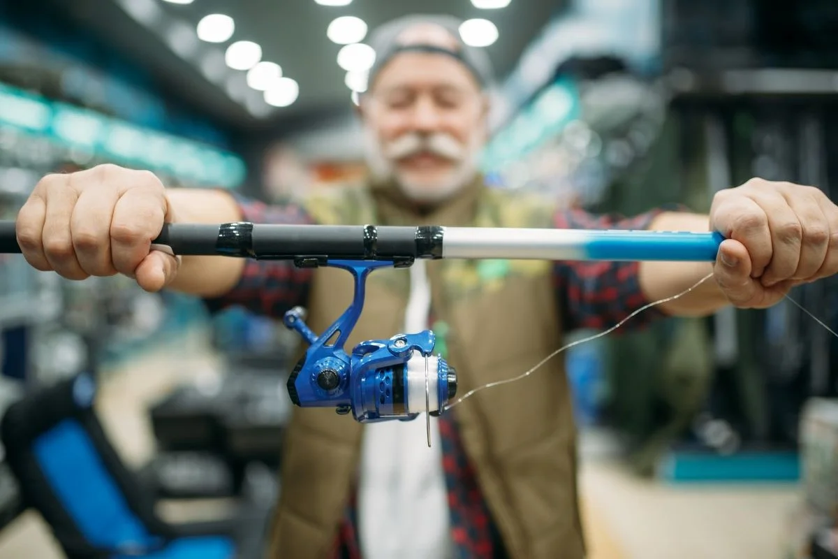 male-angler-shows-rod-with-reel-in-fishing-shop-2023-11-27-05-26-05-utc
